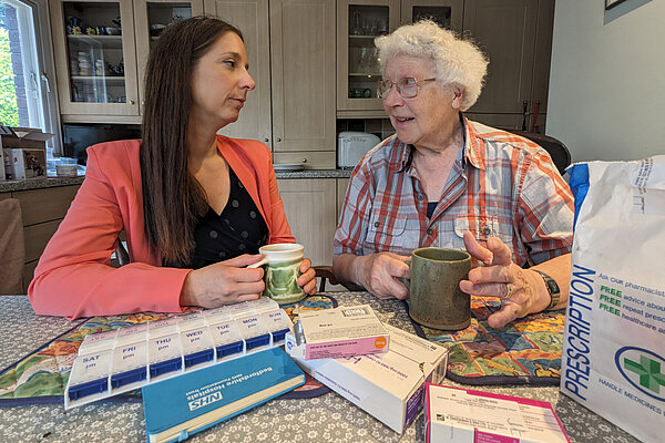 Emma Holland-Lindsay in conversation with a woman. Foreground shows boxes for medication from a pharmacy.